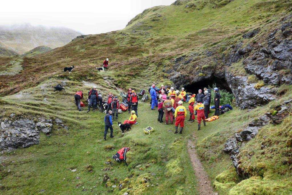 A group of people standing near the entrance to a cave on the side of a mountain